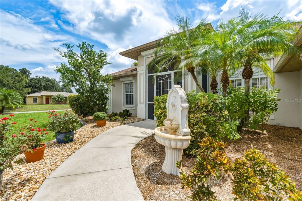 A concrete walkway leads to a house entrance with a stone fountain and palm trees — 2336 BRIARWOOD STREET, PUNTA GORDA, FL