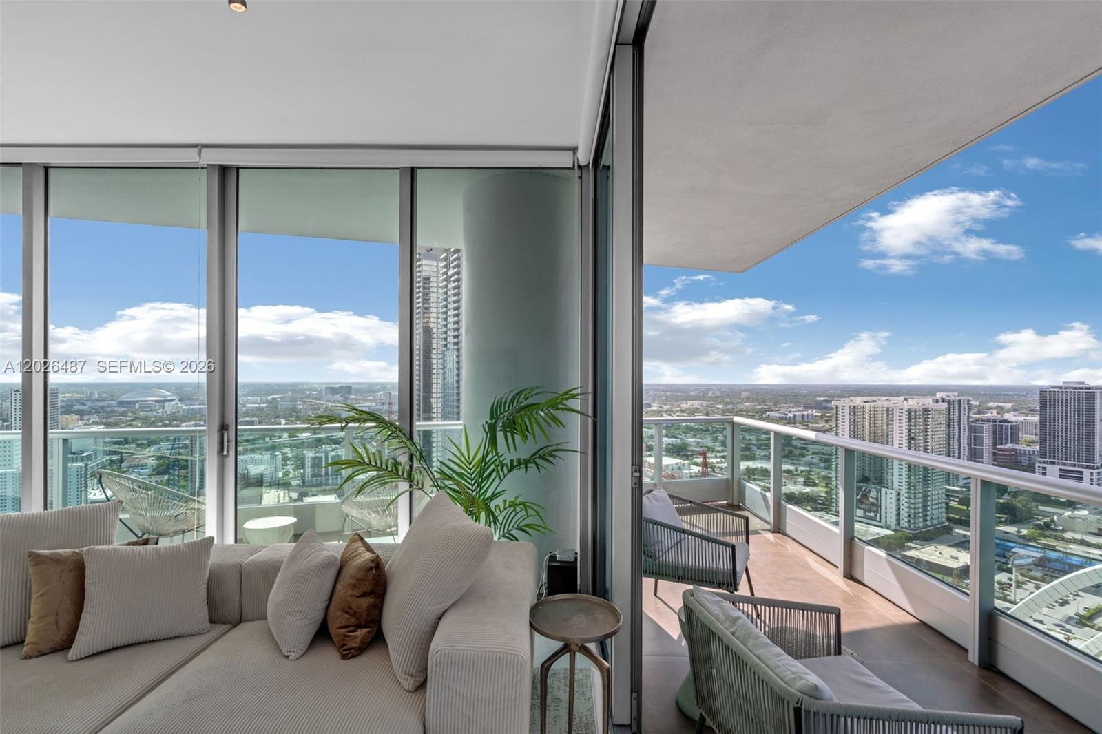 A living room with a beige sofa opens to a balcony overlooking a city skyline — 900 Biscayne Blvd # 4412, Miami FL 33132, MIAMI, FL