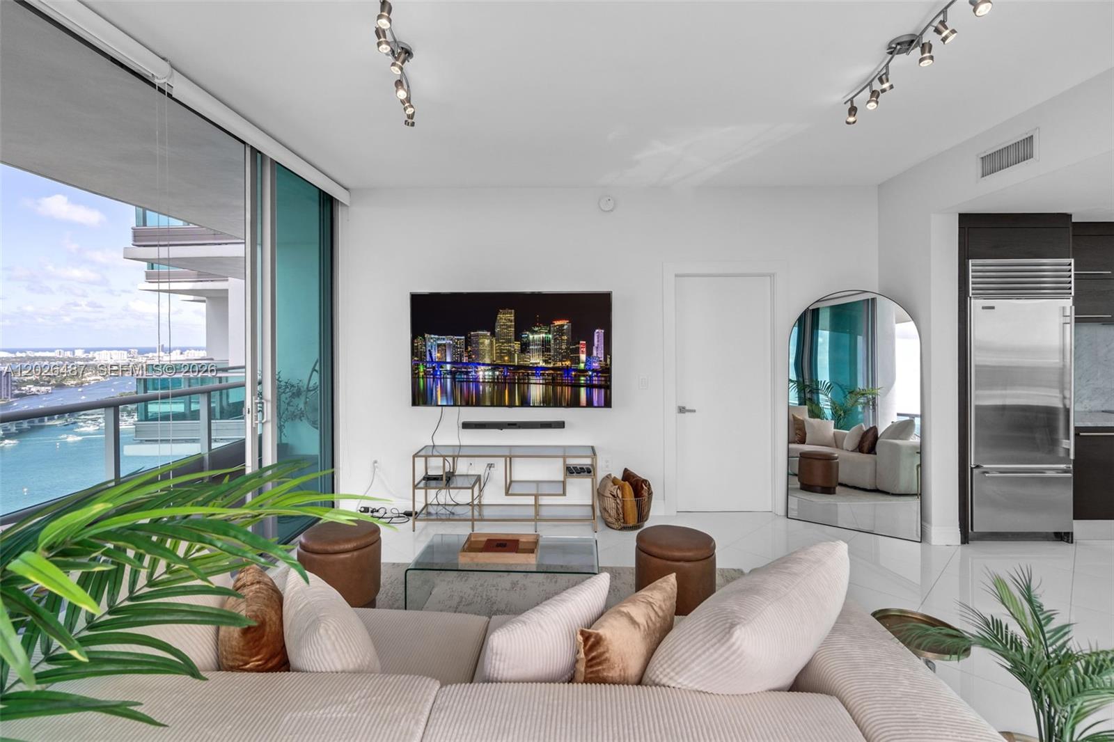 A modern living room features a wall-mounted television, glass console, arched mirror, and balcony view — 900 Biscayne Blvd # 4412, Miami FL 33132, MIAMI, FL