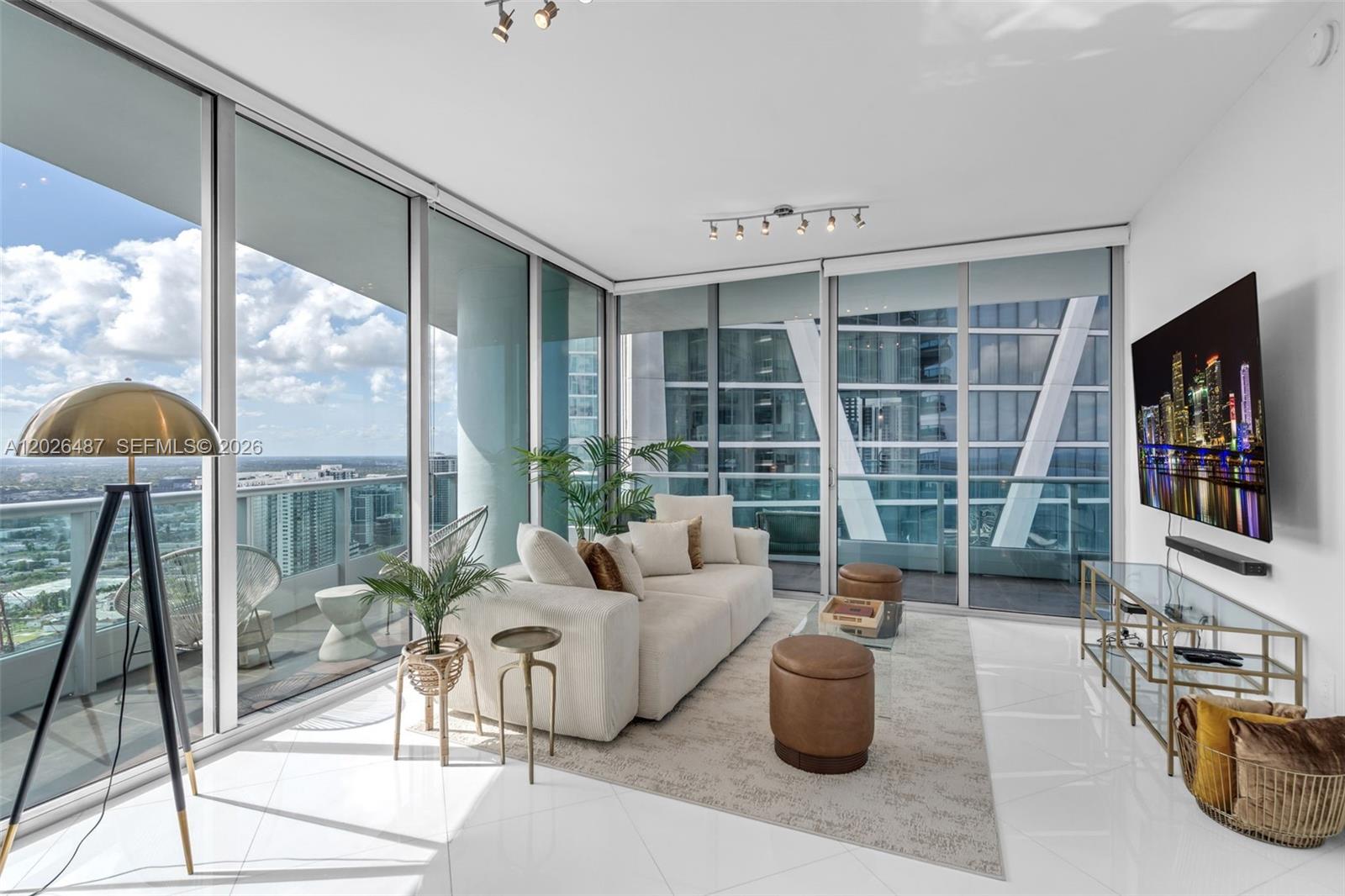 A modern living room features white tile floors, a beige sofa, and floor-to-ceiling glass walls — 900 Biscayne Blvd # 4412, Miami FL 33132, MIAMI, FL