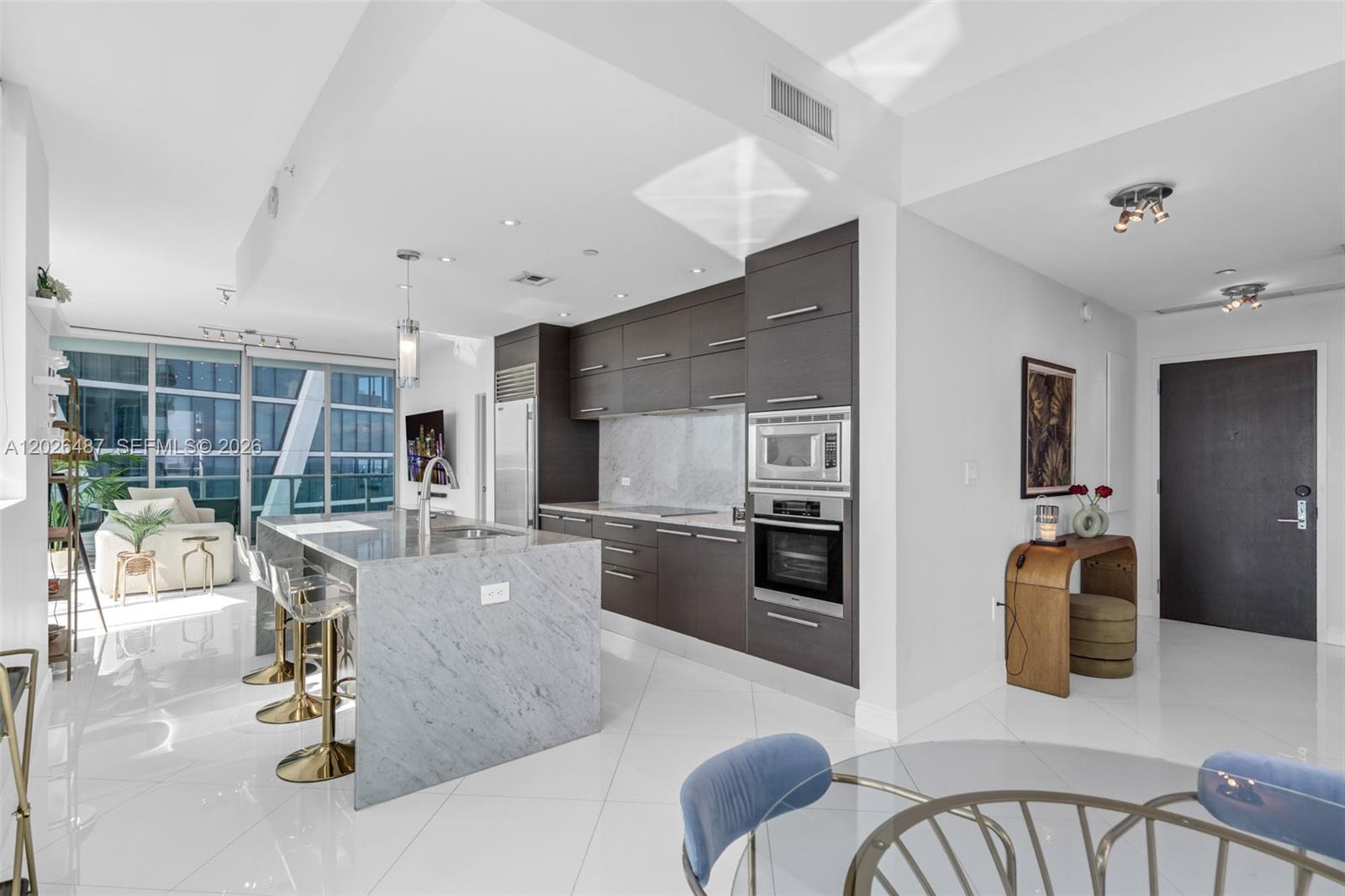 A modern kitchen features a marble island, dark wood cabinetry, and white tile flooring — 900 Biscayne Blvd # 4412, Miami FL 33132, MIAMI, FL