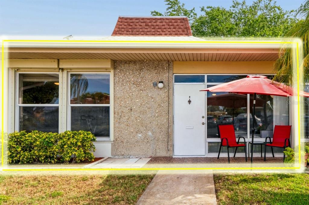 The exterior of a single-story home features a white door, large windows, and red chairs — 4363 TAHITIAN GARDENS CIRCLE UNIT B, HOLIDAY, FL