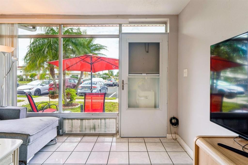 A sunroom with white tile floors, a glass door, and large windows overlooking a parking lot — 4363 TAHITIAN GARDENS CIRCLE UNIT B, HOLIDAY, FL