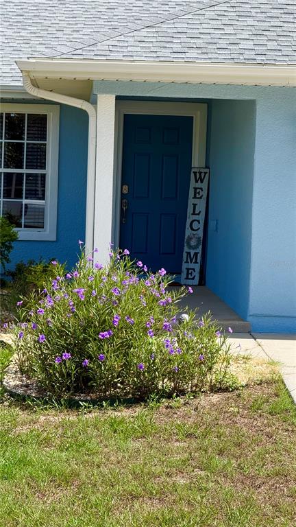 A blue front door with a welcome sign sits under a covered entryway beside landscaping — 10365 SE 148TH STREET, SUMMERFIELD, FL
