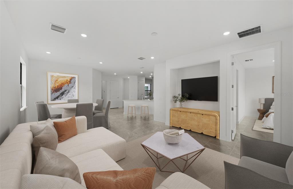 A modern living room features a sectional sofa, a television, and an open-concept dining area — 18604 HARBOR SANDS PLACE, LAKEWOOD RANCH, FL