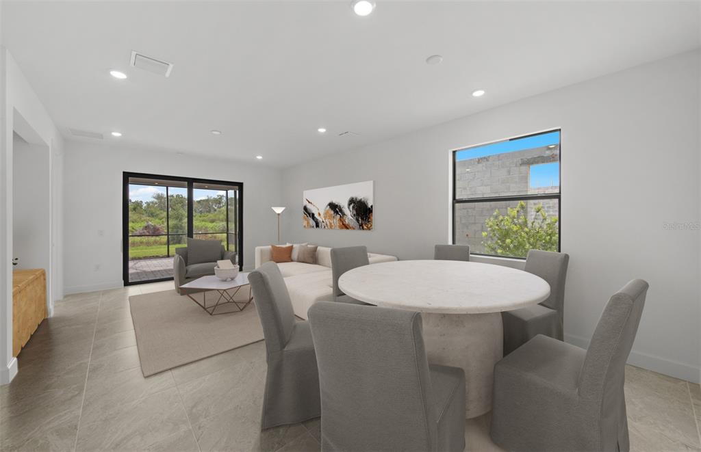 An open-concept living and dining area features tile flooring, a round table, and sliding doors — 18604 HARBOR SANDS PLACE, LAKEWOOD RANCH, FL