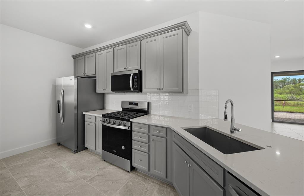 A kitchen with gray cabinets, stainless steel appliances, white countertops, and a tile backsplash — 18604 HARBOR SANDS PLACE, LAKEWOOD RANCH, FL