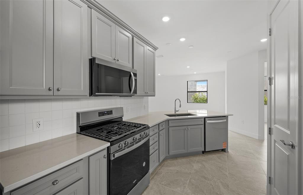 A kitchen features grey cabinets, stainless steel appliances, light countertops, and tile flooring — 18604 HARBOR SANDS PLACE, LAKEWOOD RANCH, FL