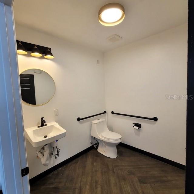 A modern, accessible bathroom features a white pedestal sink, a toilet with grab bars, and lighting — 6124 CENTRAL AVENUE, ST PETERSBURG, FL