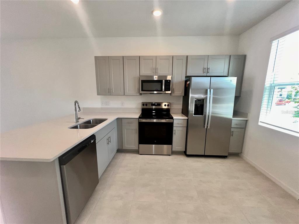 A kitchen features gray cabinets, stainless steel appliances, and a white quartz island countertop — 3200 SKYLINE LOOP, KISSIMMEE, FL