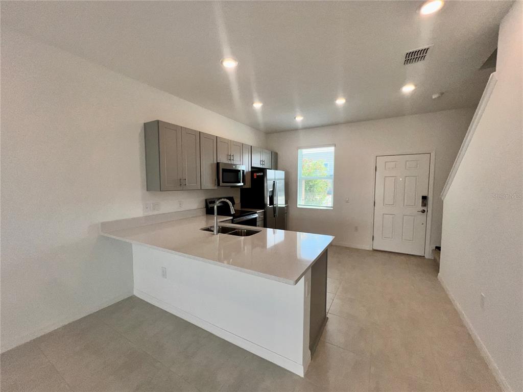 A modern kitchen features gray cabinets, a white quartz island, and stainless steel appliances — 3200 SKYLINE LOOP, KISSIMMEE, FL