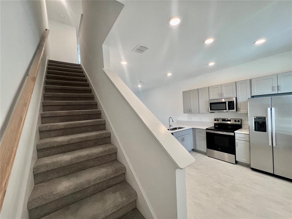 A carpeted staircase leads upward next to a modern kitchen with gray cabinets and appliances — 3200 SKYLINE LOOP, KISSIMMEE, FL