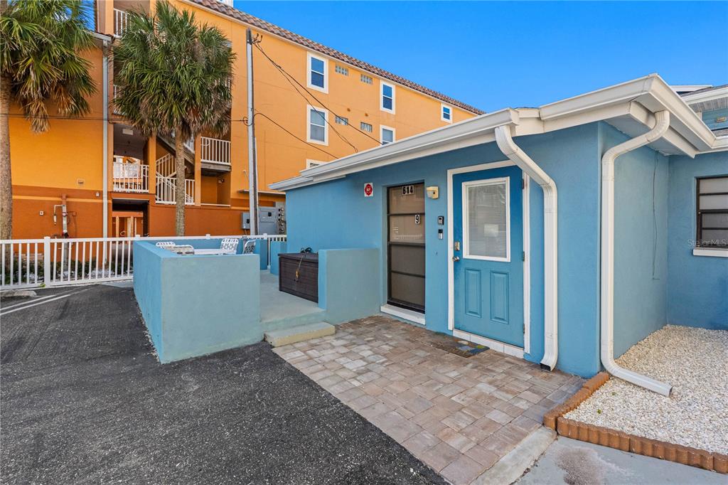 A blue exterior building features a paved patio area, a white fence, and a door — 614 GULF BOULEVARD UNIT 9, INDIAN ROCKS BEACH, FL