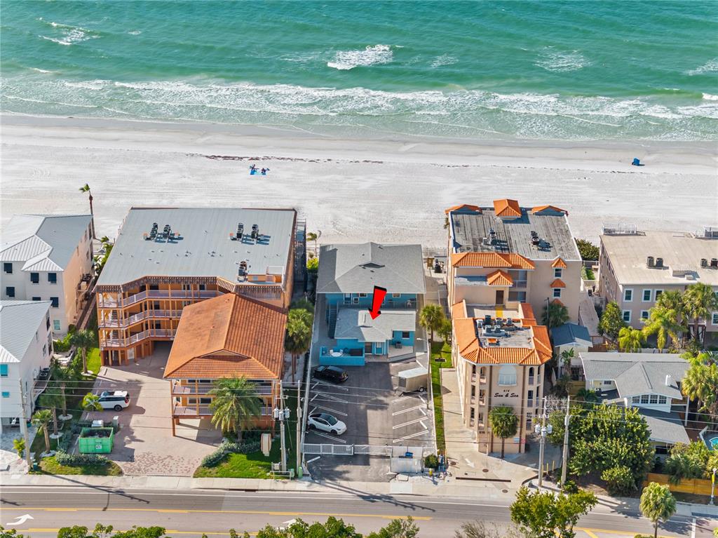 An aerial view shows a beachside property with a parking lot and surrounding buildings — 614 GULF BOULEVARD UNIT 9, INDIAN ROCKS BEACH, FL