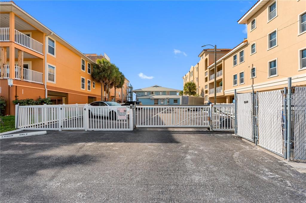 A white gate secures the entrance to a parking area between two multi-story apartment buildings — 614 GULF BOULEVARD UNIT 9, INDIAN ROCKS BEACH, FL