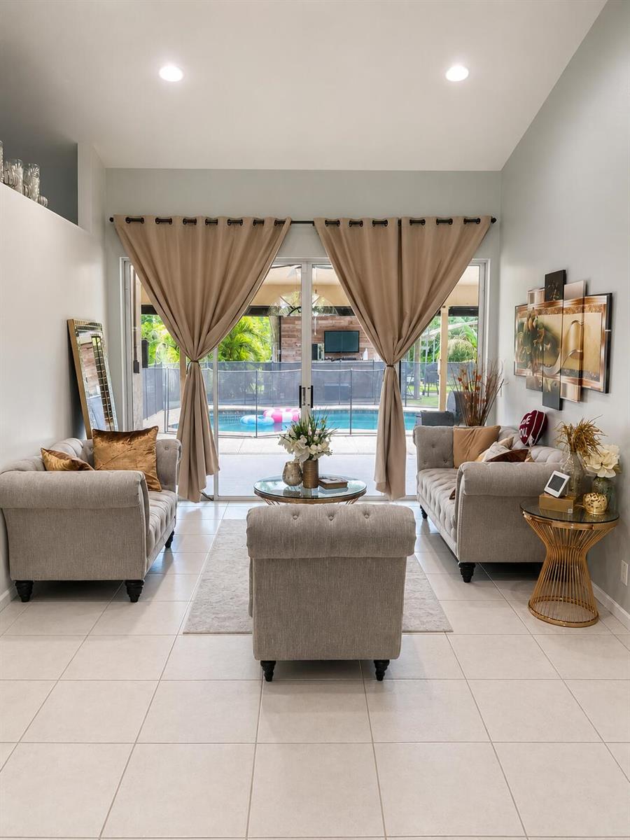 A living room with light gray sofas, a glass coffee table, and sliding doors to a pool — 18633 N 92nd Ln Lane N, FL 33470, FL