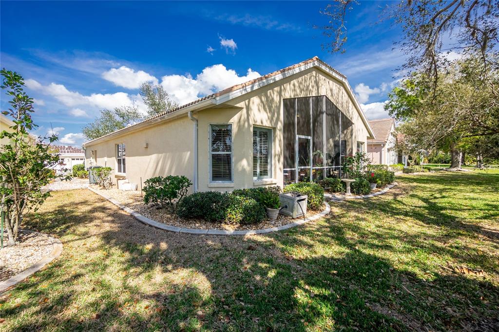 The exterior of a beige house features a screened-in lanai and landscaped garden beds — 26162 STILLWATER CIRCLE, PUNTA GORDA, FL