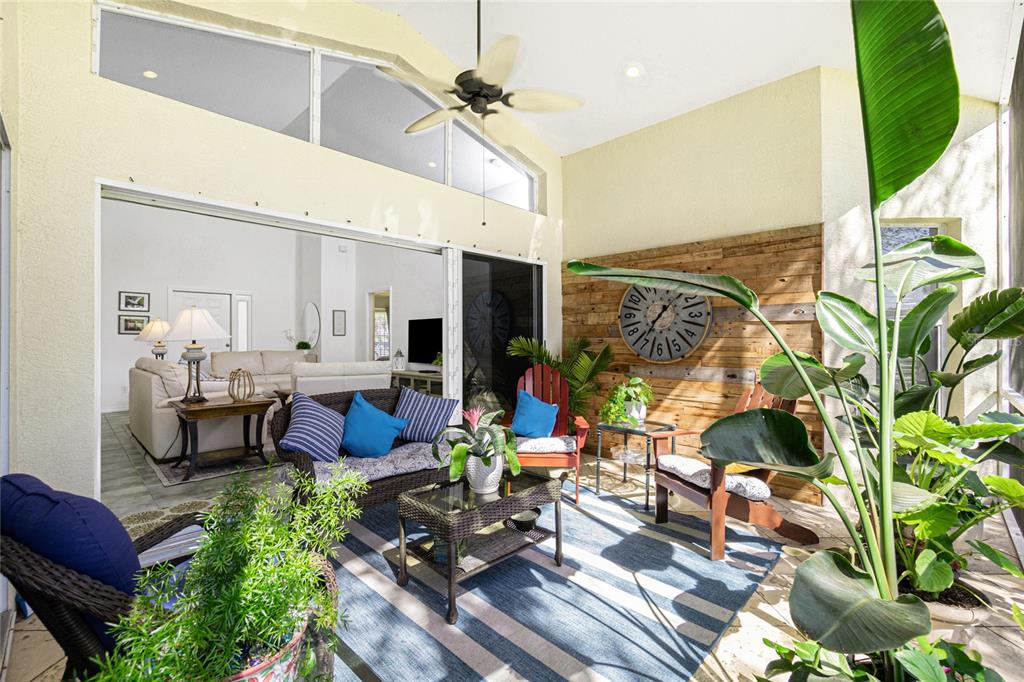 A sunroom features a wood-paneled wall, a large clock, wicker furniture, and a ceiling fan — 26162 STILLWATER CIRCLE, PUNTA GORDA, FL
