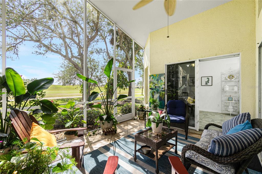 A screened-in patio features tile flooring, wicker furniture, and a view of a grassy field — 26162 STILLWATER CIRCLE, PUNTA GORDA, FL