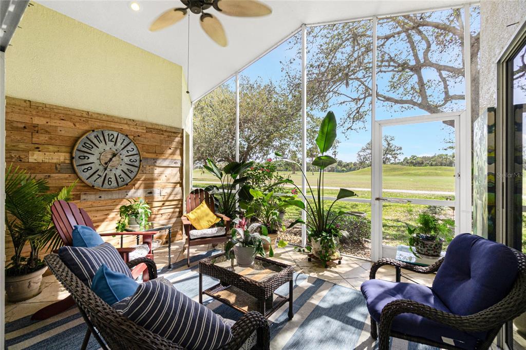 A screened-in patio features wicker furniture, a large wall clock, and views of a golf course — 26162 STILLWATER CIRCLE, PUNTA GORDA, FL