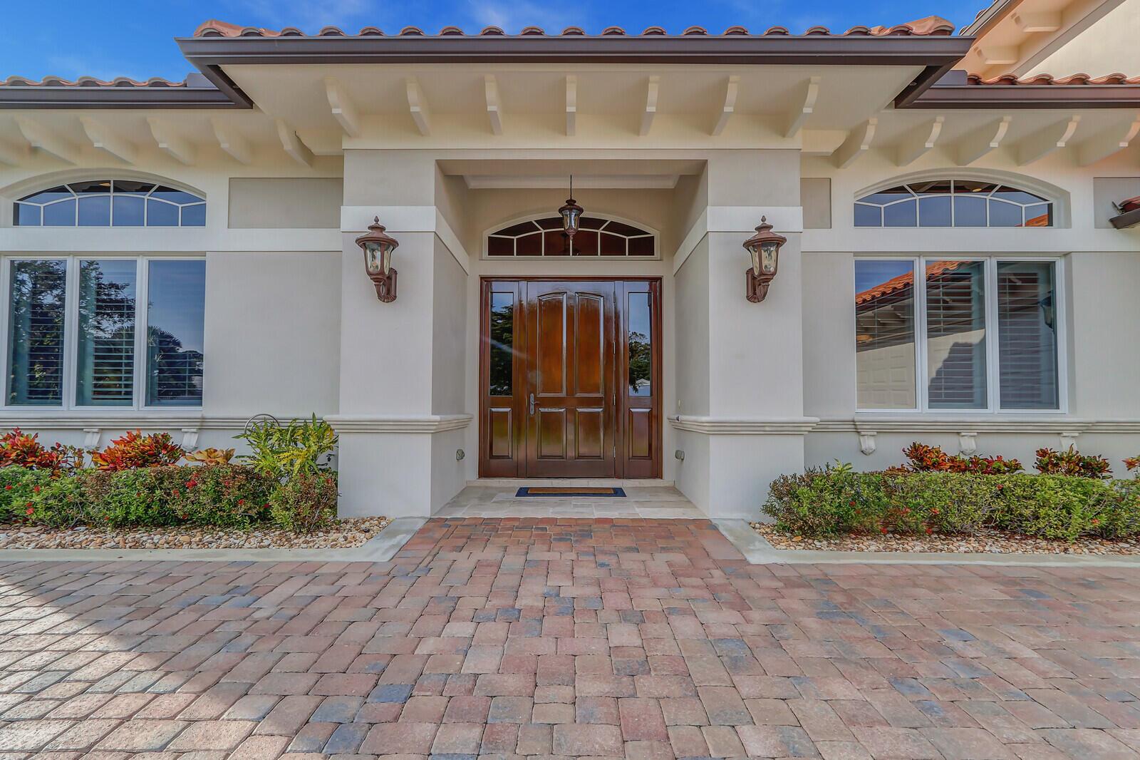 The exterior of a house features a brick paver driveway, a wooden front door, and landscaping — 3572 SE Court Drive, Stuart FL 34997, STUART, FL