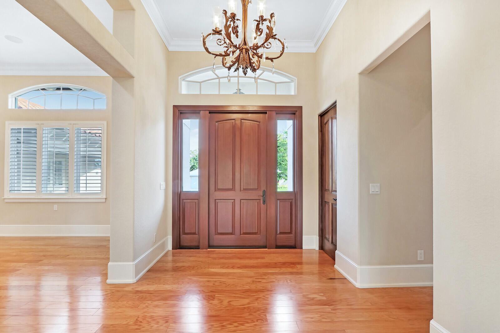 A foyer features hardwood floors, a wooden front door with sidelights, and a hanging chandelier — 3572 SE Court Drive, Stuart FL 34997, STUART, FL