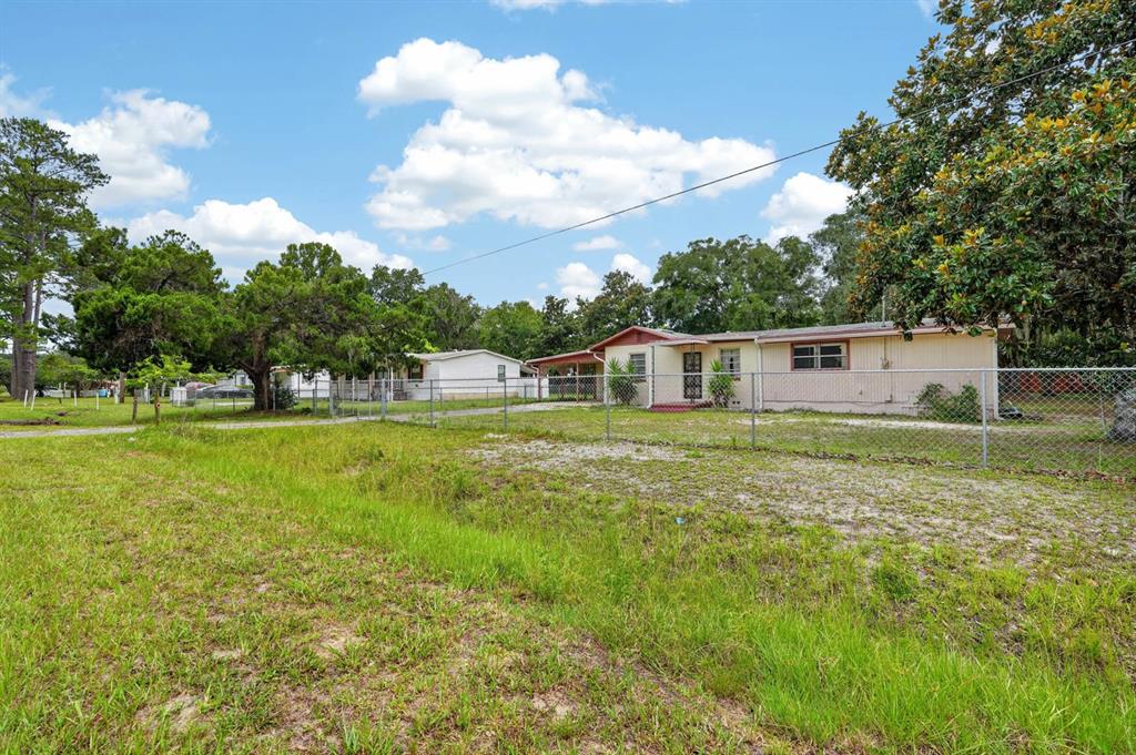 A single-story house with a chain-link fence sits on a grassy lot under a sky — 131 DUNN AVENUE, SAN MATEO, FL