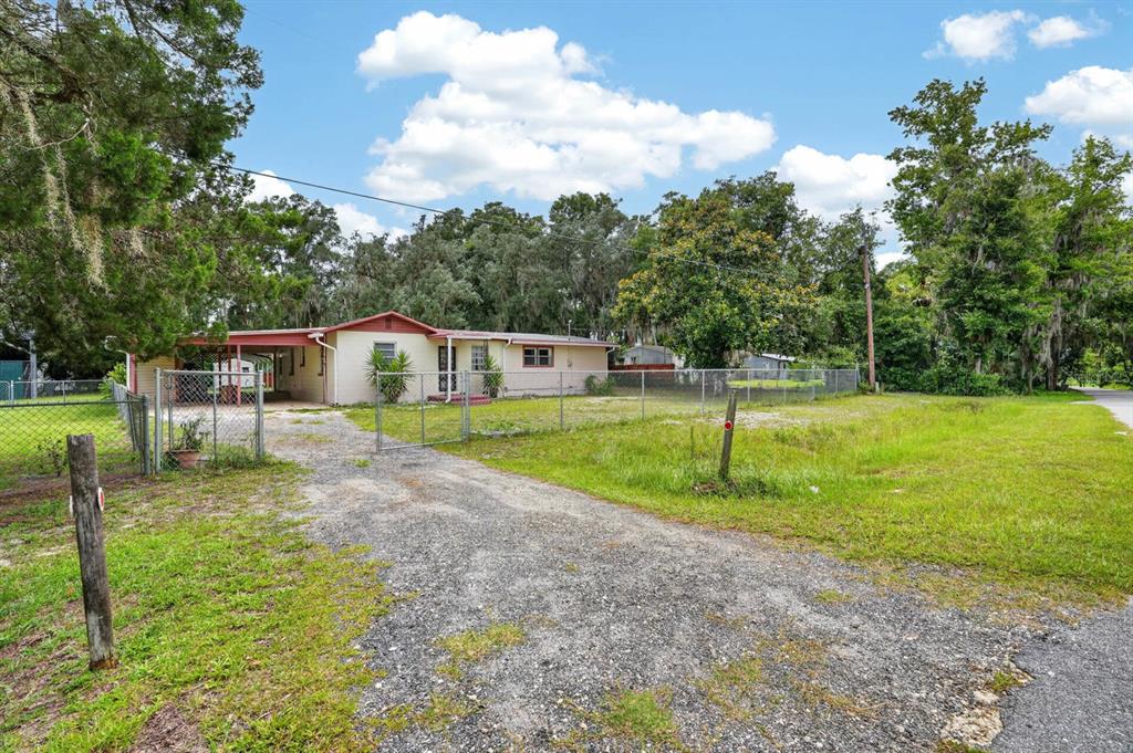 A single-story house with a carport sits behind a chain-link fence on a gravel lot — 131 DUNN AVENUE, SAN MATEO, FL