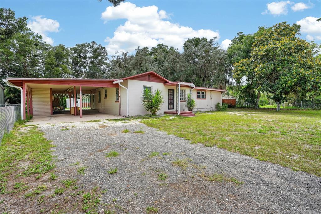 A single-story house with a gravel driveway, attached carport, and a large grassy yard — 131 DUNN AVENUE, SAN MATEO, FL