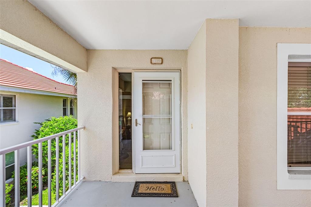 A white front door with a storm door and a welcome mat on a balcony — 14008 WILLOW GLEN COURT UNIT 210, PORT CHARLOTTE, FL