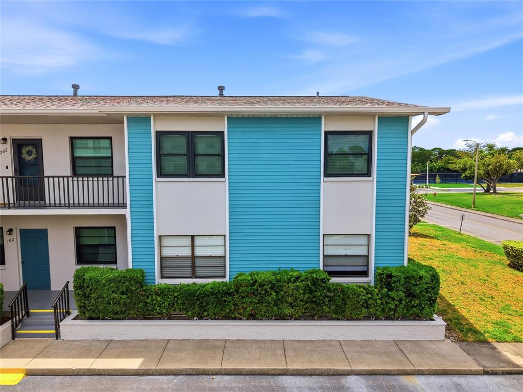 A two-story apartment building exterior features teal siding, white stucco walls, and a green hedge — 5967 TERRACE PARK DRIVE N UNIT 201, ST PETERSBURG, FL