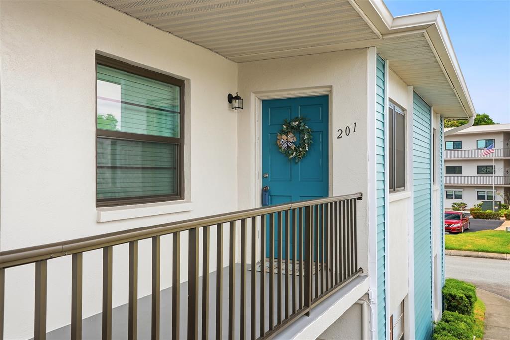 An exterior view of a second-story apartment balcony with a blue front door numbered 201 — 5967 TERRACE PARK DRIVE N UNIT 201, ST PETERSBURG, FL