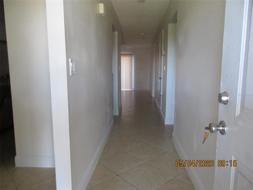 A hallway with light-colored walls and diagonal tile flooring leads toward a sliding glass door — 2112 BAHAMAS COURT, KISSIMMEE, FL