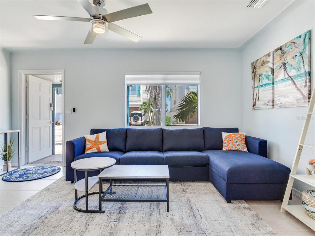A living room features a blue sectional sofa, a coffee table, and a ceiling fan — 230 144TH AVENUE, MADEIRA BEACH, FL
