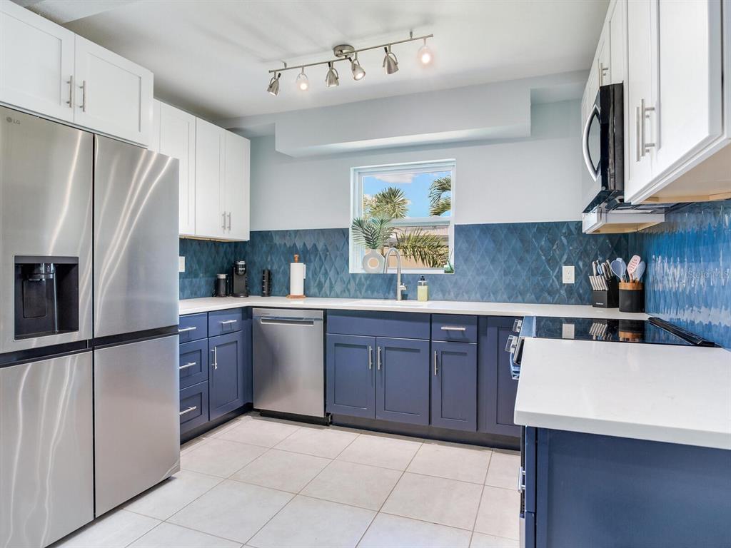 A kitchen features blue lower cabinets, white upper cabinets, stainless steel appliances, and blue tile — 230 144TH AVENUE, MADEIRA BEACH, FL