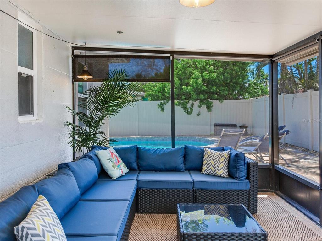 A screened-in patio features a blue sectional sofa, a glass-top table, and a swimming pool — 230 144TH AVENUE, MADEIRA BEACH, FL