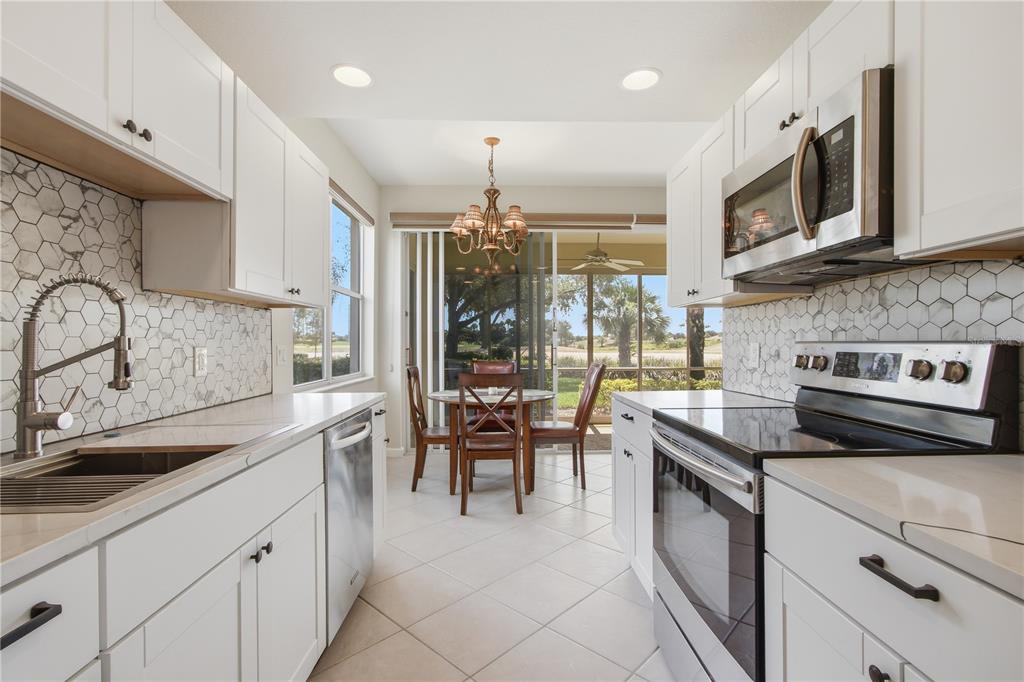 A galley kitchen with white cabinets, marble hexagon backsplash, and stainless appliances leads to a dining area — 3010 MEANDERING WAY UNIT 101, FORT MYERS, FL
