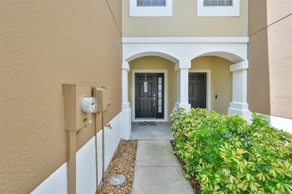 A concrete walkway leads to the front entrance of a tan townhouse with two doors — 10141 POST HARVEST DRIVE, RIVERVIEW, FL