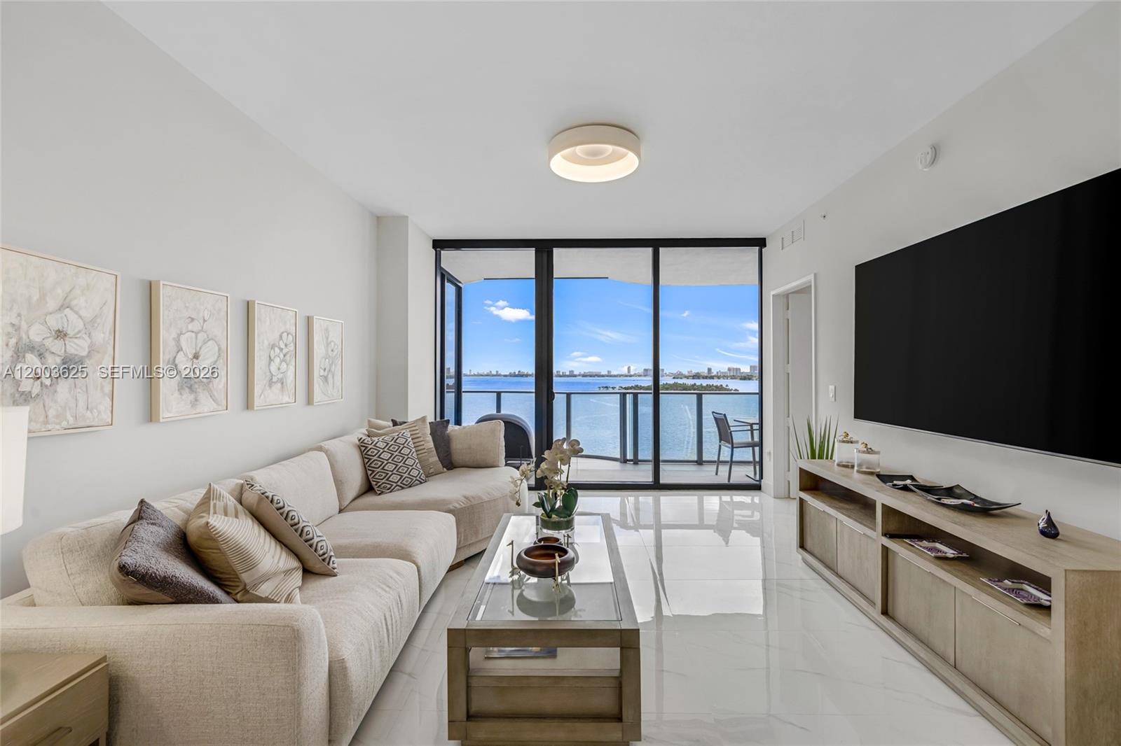 A modern living room features a beige sectional sofa, glass coffee table, and waterfront balcony view — 711 NE 23 # 704, Miami FL 33137, MIAMI, FL