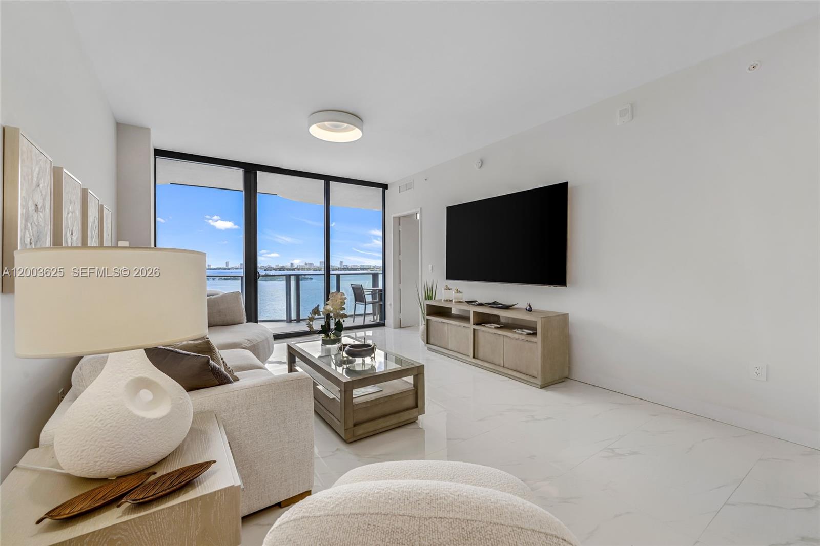 A living room features white tile floors, a wall-mounted television, and floor-to-ceiling balcony windows — 711 NE 23 # 704, Miami FL 33137, MIAMI, FL