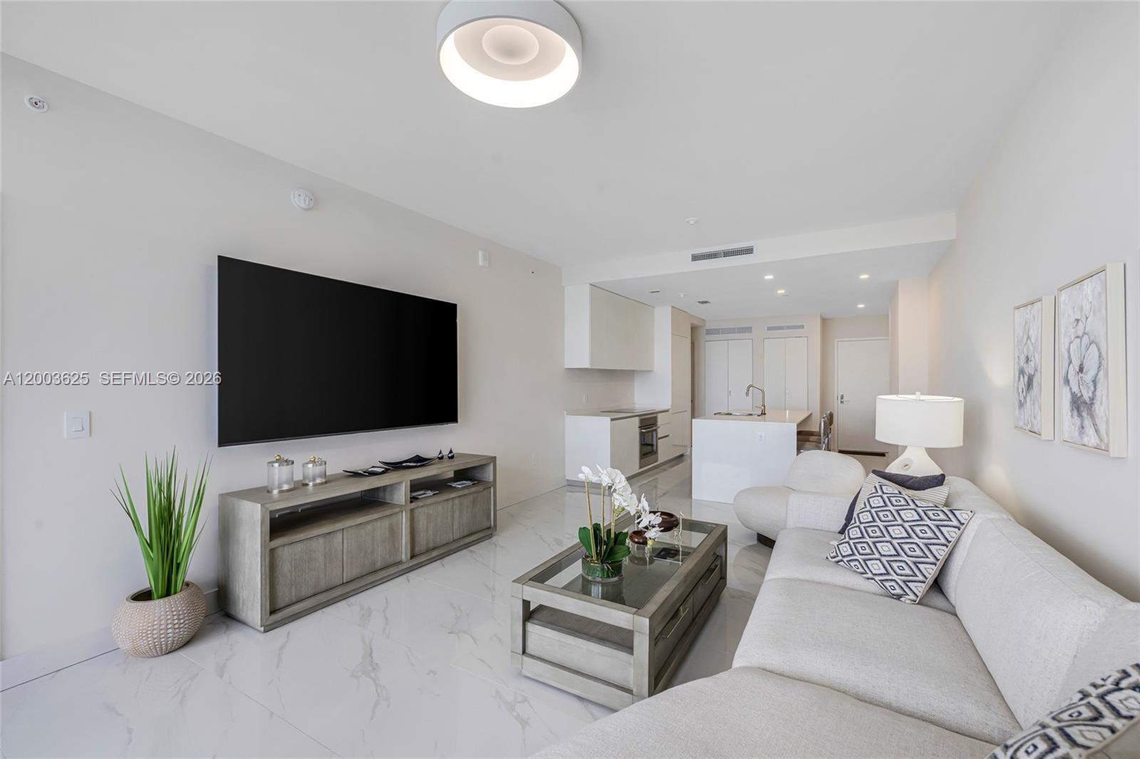 A modern living room features a large television, neutral furniture, and white marble flooring — 711 NE 23 # 704, Miami FL 33137, MIAMI, FL