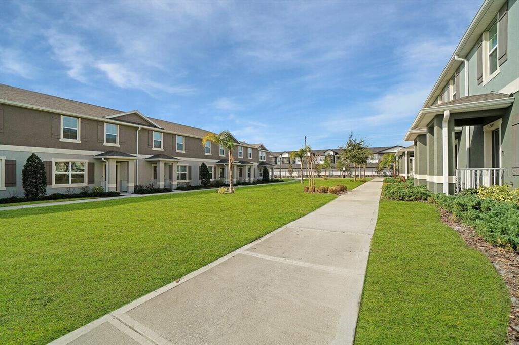 A concrete walkway separates two rows of multi-story townhomes with green lawns and blue skies — 2607 HARRIER COURT UNIT Sunset, APOPKA, FL