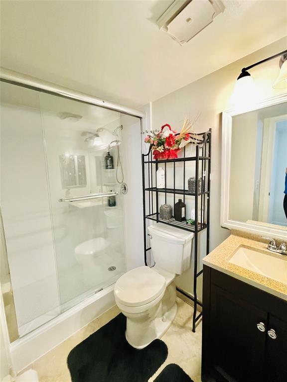 A bathroom features a glass-enclosed shower, a toilet with a metal storage rack, and a vanity — 7505 W Atlantic Boulevard # 208, Margate FL 33063, MARGATE, FL