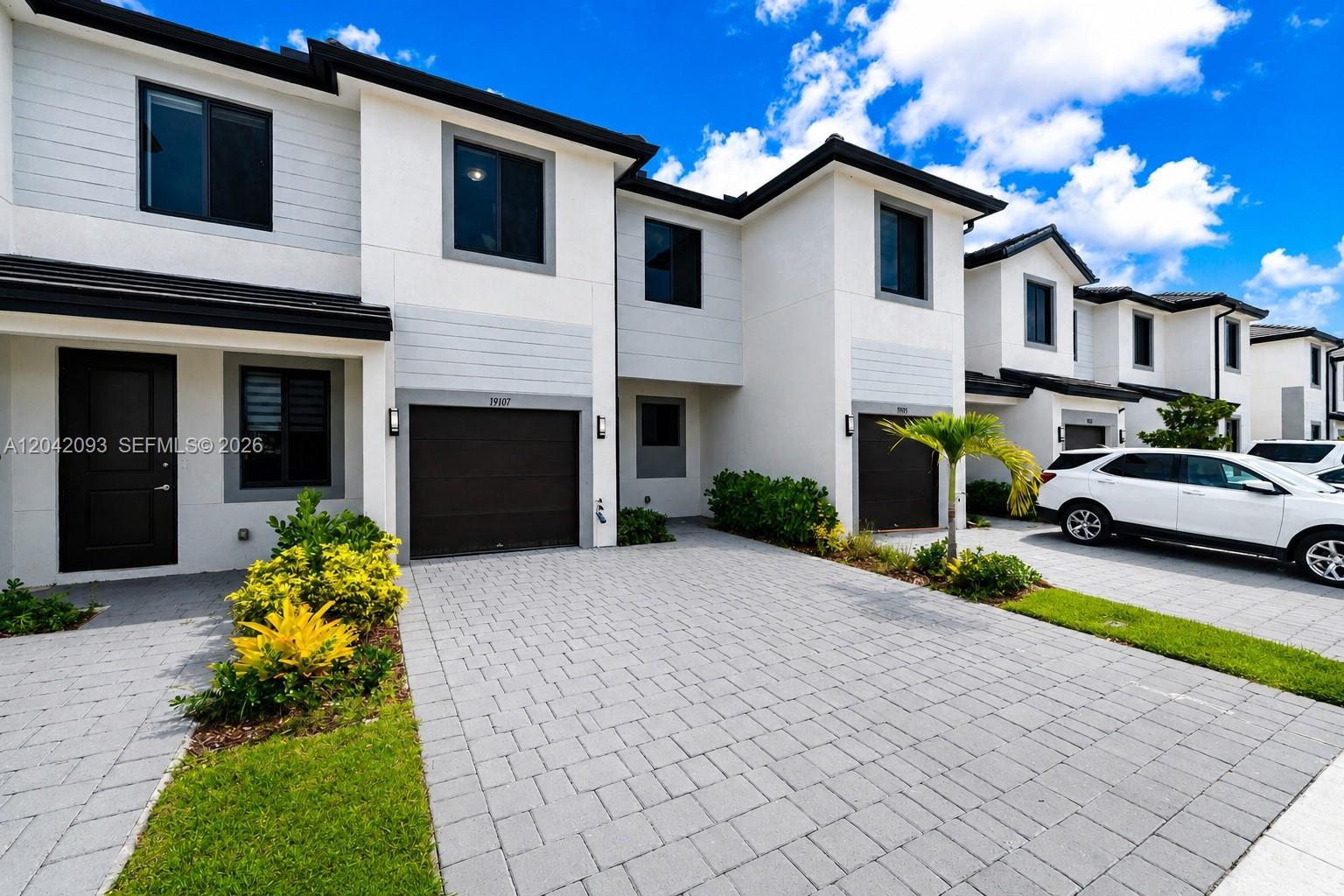 A row of modern two-story townhouses features white stucco exteriors, dark garage doors, and paved driveways — 19107 SW 344th Ter, Homestead FL 33034, HOMESTEAD, FL