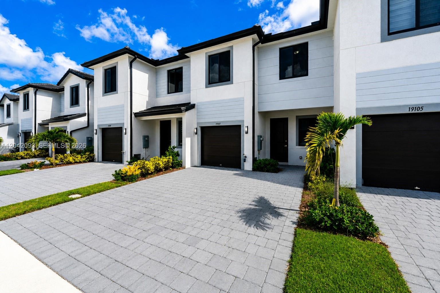 A row of modern two-story townhouses with white facades, dark garage doors, and paved driveways — 19107 SW 344th Ter, Homestead FL 33034, HOMESTEAD, FL