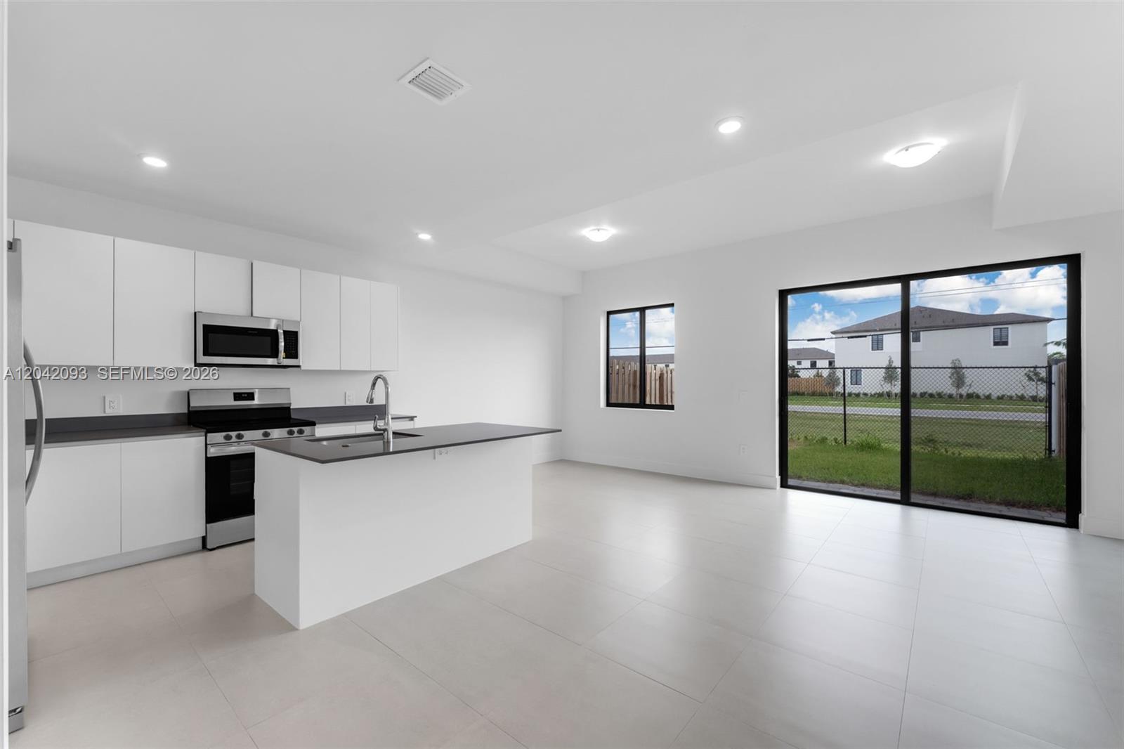 A modern kitchen with white cabinets and a dark island opens to a living area — 19107 SW 344th Ter, Homestead FL 33034, HOMESTEAD, FL