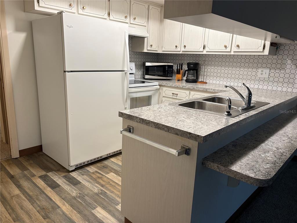 A kitchen features white cabinets, a white refrigerator, a gray countertop, and a tiled backsplash — 5433 PALM DRIVE, NEW PORT RICHEY, FL