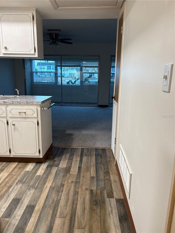A kitchen with wood-look flooring and white cabinets opens into a carpeted living area — 5433 PALM DRIVE, NEW PORT RICHEY, FL