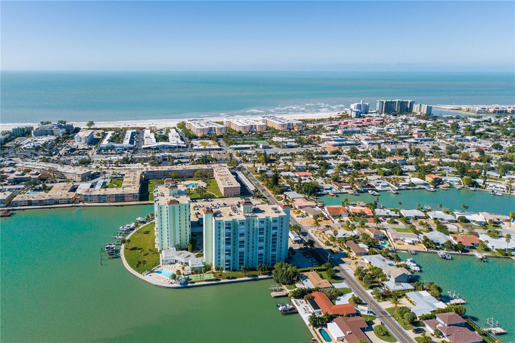 An aerial view of a coastal town featuring high-rise condominiums, residential homes, and waterfront docks — 420 64TH AVENUE UNIT 1103, ST PETE BEACH, FL