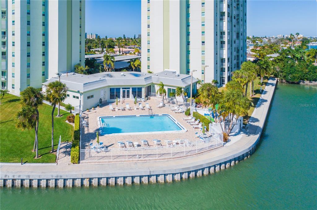An aerial view of a swimming pool and patio area next to a waterfront apartment building — 420 64TH AVENUE UNIT 1103, ST PETE BEACH, FL